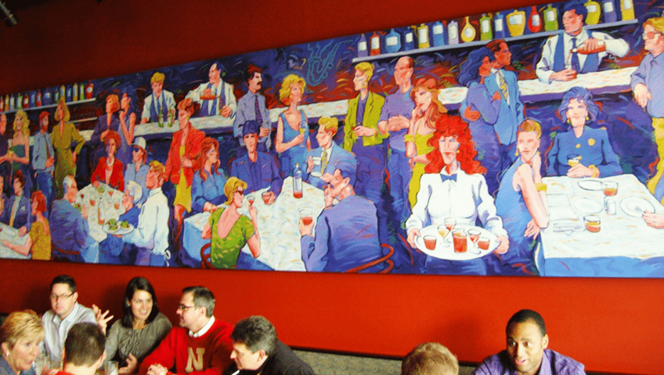 Colorful mural of a crowded bar scene with a painting above them hanging on a red color wall