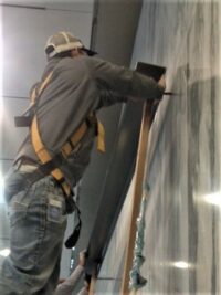 person in protective gear, likely a construction worker or renovator, installing or working on drywall or wall panels