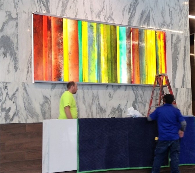 2 person, likely an artist or installer, working on hanging a large, colorful abstract artwork with vertical stripes on a wall